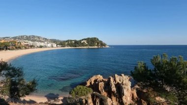 Sakin dalgalarla deniz kıyısı manzarası, berrak mavi gökyüzü ve tepenin üzerinden biraz yeşillik