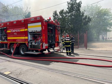 Bucharest, Romania - 05.07.2022: fire engine in a residential area with firefighters nearby extinguishing a burning abandoned building
