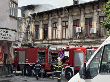 Bucharest, Romania - 05.07.2022: fire engine in a residential area with firefighters nearby extinguishing a burning abandoned building