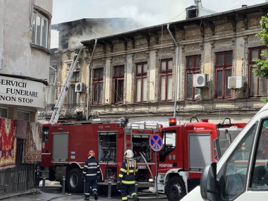 Bucharest, Romania - 05.07.2022: fire engine in a residential area with firefighters nearby extinguishing a burning abandoned building