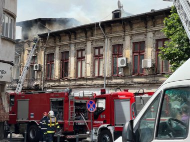 Bucharest, Romania - 05.07.2022: fire engine in a residential area with firefighters nearby extinguishing a burning abandoned building