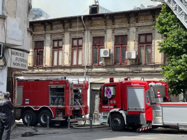 Bucharest, Romania - 05.07.2022: fire engine in a residential area with firefighters nearby extinguishing a burning abandoned building