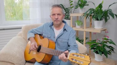 Son sınıf öğrencisi akustik gitar çalıyor ve apartman dairesinde şarkı söylüyor.