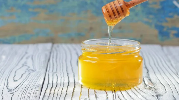 De glazen pot met verse honing op de rustieke achtergrond. Honingachtergrond — Stockfoto