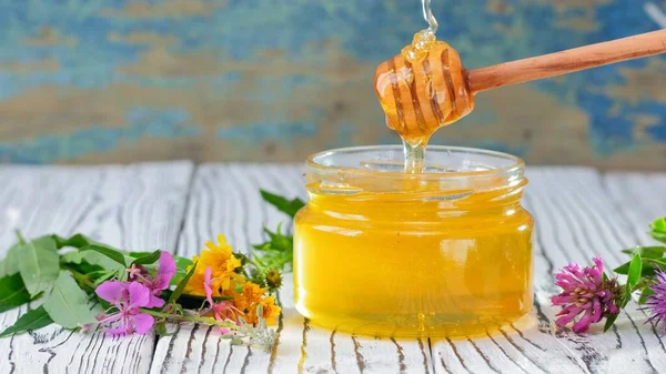 De glazen pot met verse honing op de rustieke achtergrond. Bloemen op tafel. — Stockfoto
