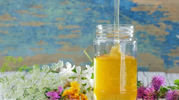 The glass jar with fresh honey on the rustic background. Flowers on the table. — Stock Photo, Image