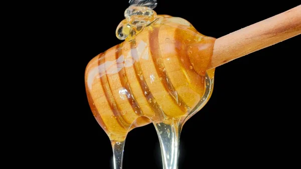 Close up fresh fluid honey pouring and flowing from wooden dipper spoon — Stock Photo, Image