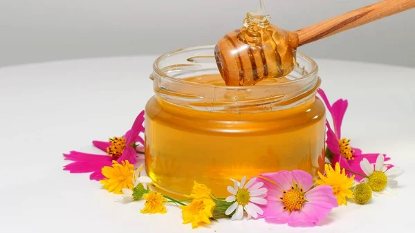 De glazen pot met verse honing op witte ondergrond. Bloemen op tafel. — Stockfoto