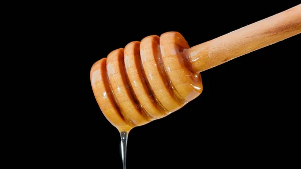 Honey pouring and flowing from wooden dipper spoon over black background — Stock Photo, Image
