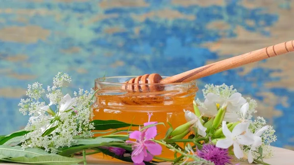 De glazen pot met verse honing op de rustieke achtergrond. Bloemen op tafel. — Stockfoto