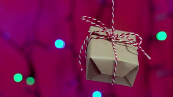 Die dekorative Geschenkschachtel, die mit einem roten Band gebunden ist, dreht sich an einem Seil — Stockvideo