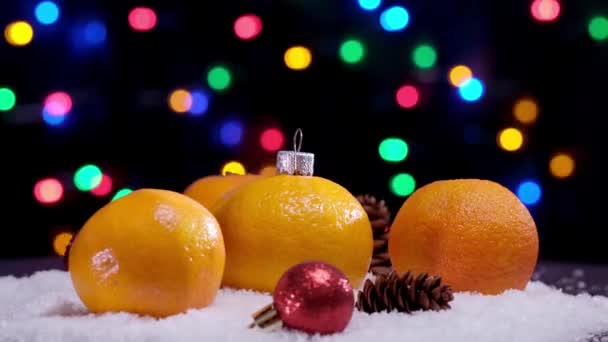 4K. Weihnachten orange Mandarinenfrüchte und rote Kugelspielzeuge auf dem Schnee Rotation — Stockvideo