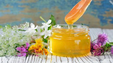 Kırsal arka planda taze bal bulunan cam kavanoz. Masada çiçekler.