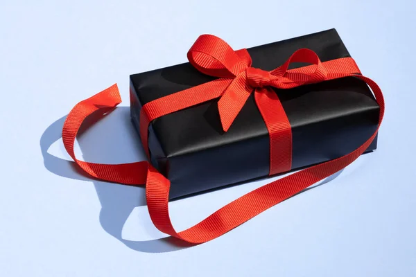 Mavi arka planda kırmızı kurdeleli siyah hediye kutusu. Kırmızı kurdeleli hediye kutusu.. — Stok fotoğraf
