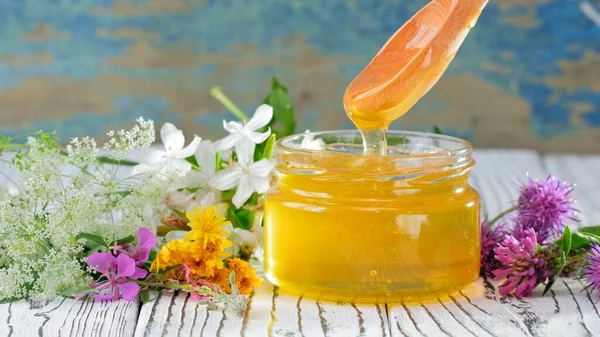 Kırsal arka planda taze bal bulunan cam kavanoz. Masada çiçekler.