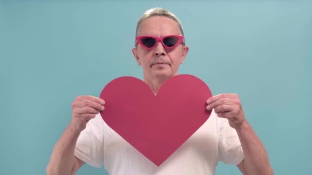 Smilende alderen mand viser stort rødt hjerte isoleret blå farve baggrund. – Stock-video