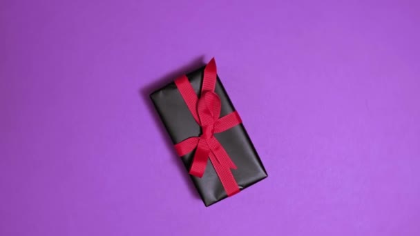 4k. Forgó ajándékdoboz fekete ajándékpapírba csomagolva piros szalaggal — Stock videók