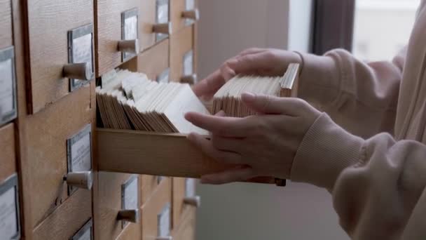 Catálogo de tarjetas en la biblioteca. Mujer está buscando información en un gabinete de archivos — Vídeos de Stock