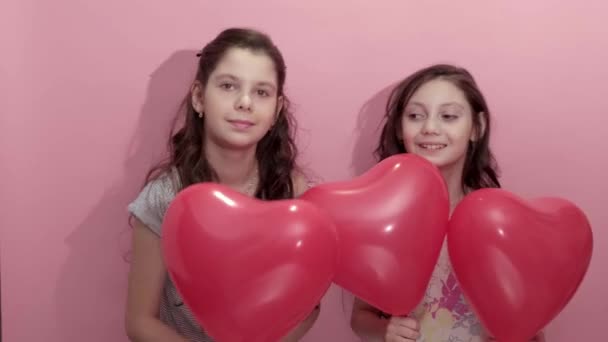 4K. Filles mignonnes sœurs avec des ballons coeur rouge sur fond rose. — Video