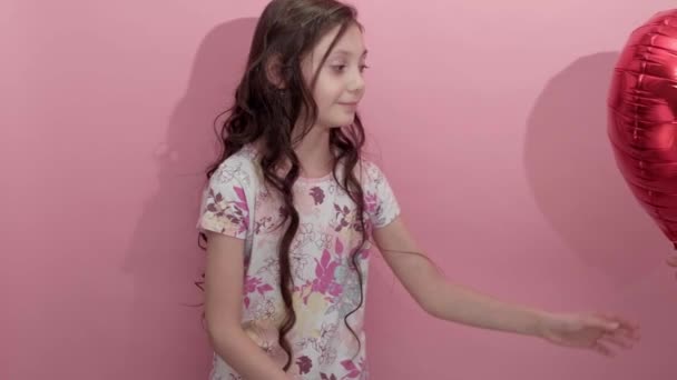 Beautiful girl on a pink background with a red balloon in the shape of a heart — Stock Video