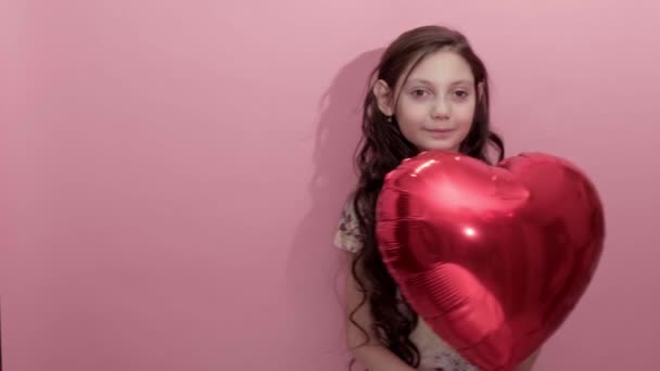 Pembe arka planda, kalp şeklinde kırmızı bir balonu olan güzel bir kız. — Stok video