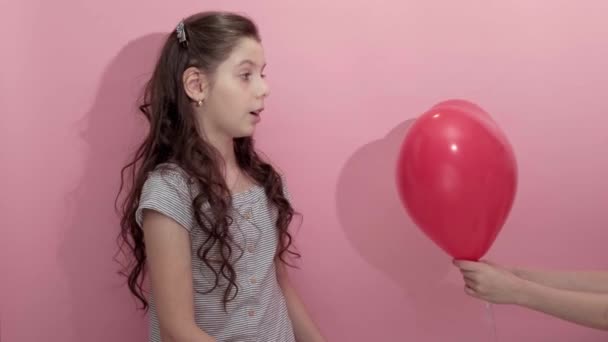 Krásná dívka na růžovém pozadí s červeným balónem ve tvaru srdce — Stock video