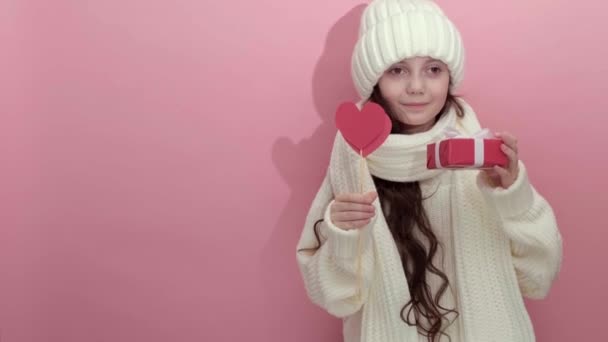 Ευτυχισμένο νεαρό κορίτσι φορώντας λευκό πλεκτό πουλόβερ κρατώντας κόκκινες καρδιές πάνω από τα μάτια — Αρχείο Βίντεο