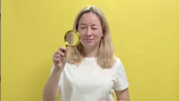 Молода жінка в білій футболці розглядає деталі через збільшувальне скло — стокове відео