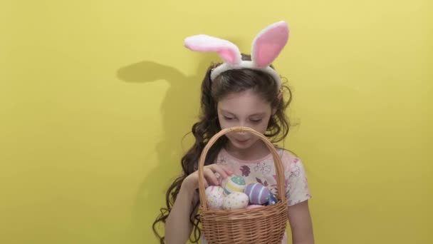 Mooi schattig klein meisje in paashaas oren houdt een mand met eieren — Stockvideo