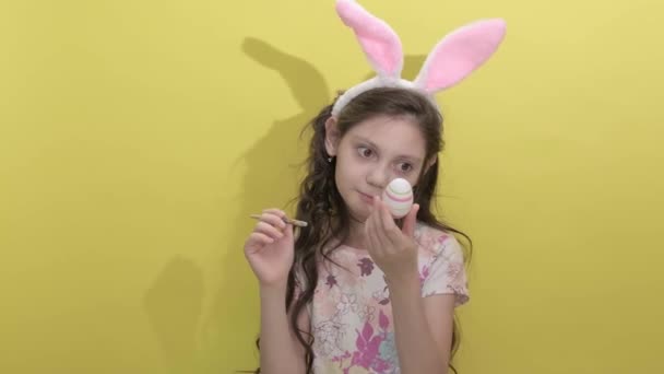 一只兔子耳朵里的小女孩在黄色的背景上画复活节彩蛋 — 图库视频影像