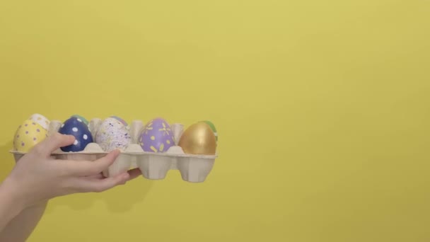 4k. Dos manos se dan huevos de Pascua sobre un fondo amarillo. — Vídeo de stock