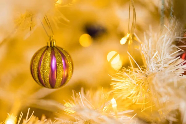 白い黄色のクリスマスツリー上の金と紫のボールのおもちゃとガーランドで休日の場所の閉鎖 — ストック写真