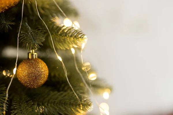 Κοντινό πλάνο του χρυσού παιχνιδιού μπάλα και γιρλάντες σε πράσινο-κίτρινο χριστουγεννιάτικο δέντρο — Φωτογραφία Αρχείου