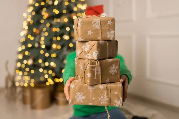 Mladá dívka drží hnědé dárky v blízkosti vánočního svátečního stromu — Stock fotografie