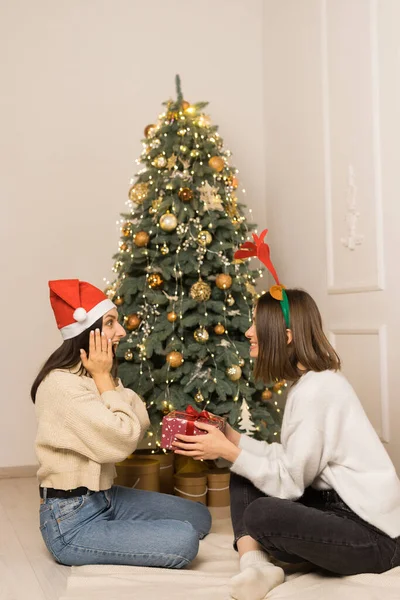 Dvě krásné dívky v bílých svetrech si dávají červený vánoční dárek — Stock fotografie