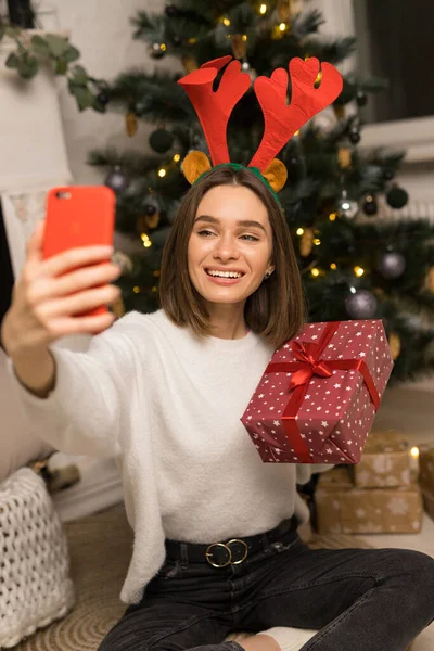 Крупним планом молода дівчина телефонує батькам і показує червоний різдвяний подарунок Ліцензійні Стокові Зображення