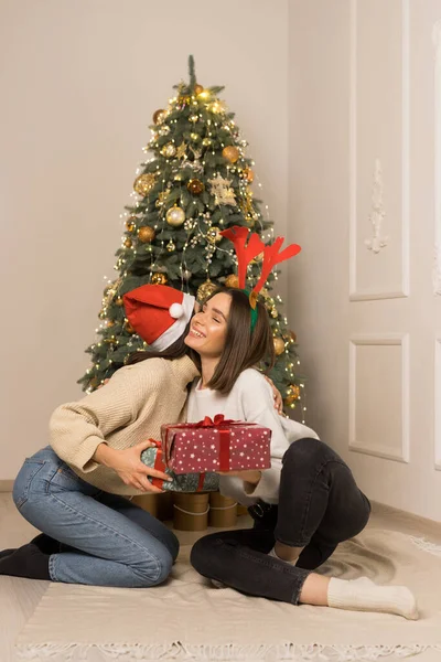 Duas meninas bonitas em blusas brancas se beijam e mantêm presentes de Natal vermelhos e verdes — Fotografia de Stock