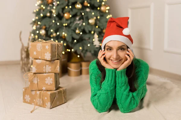 Молода усміхнена дівчина лежить біля різдвяної святкової ялинки і коричневих подарунків Ліцензійні Стокові Фото