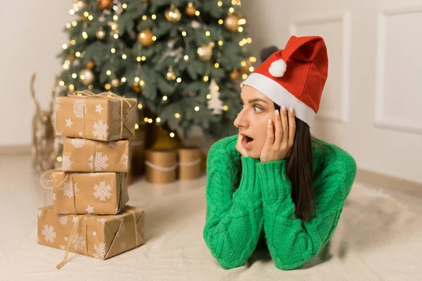 Mladá překvapená dívka ležící poblíž vánoční slavnostní strom a hnědé dárky — Stock fotografie