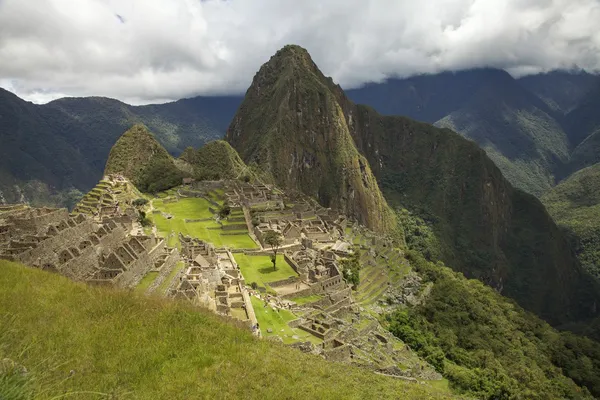 Tradicional y típica vista de Machu Picchu. Sol asomándose a través del cielo nublado . — Foto de Stock