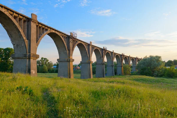 Bir yaz akşamı yeşil bir vadi üzerinde uzun kemerli bir demiryolu köprüsü.
