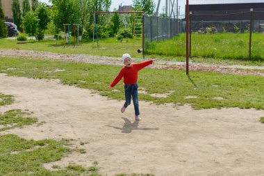 Kırmızı elbiseli gülümseyen bir çocuk özel bir evin bahçesinde kollarını açmış koşar.