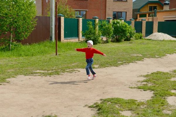 Kırmızı elbiseli gülümseyen bir çocuk özel bir evin bahçesinde kollarını açmış koşar.