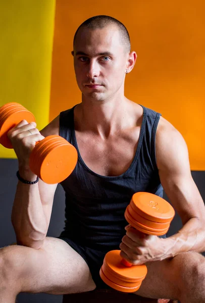 a strong athletic man holding orange dumbbells orange and yellow background photo