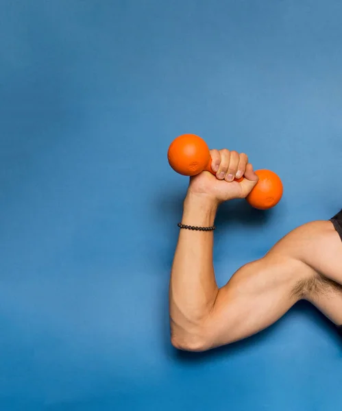 orange dumbbell in a strong male hand blue background photo