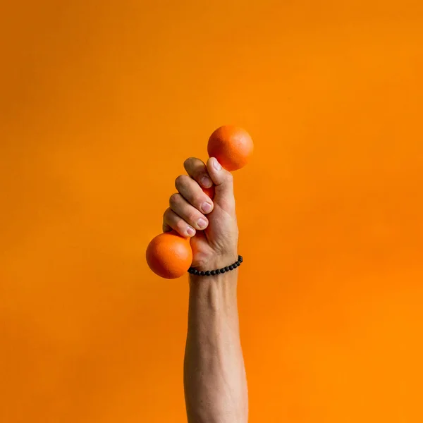 photo of an orange small dumbbell in a male hand background orange