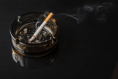 Siyah ayna yüzeyinde kahverengi cam bir kül tablasında sigara yaktım.