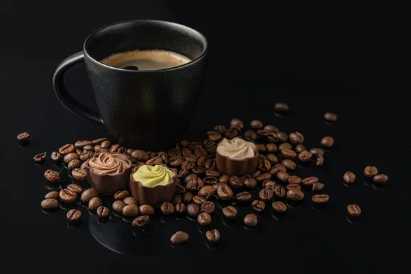 黒のセラミックカップにコーヒー豆と黒のガラスの表面にグルメチョコレートのお菓子 — ストック写真