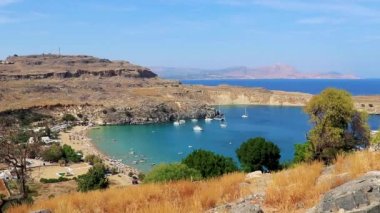 Lindos Sahili panorama manzarası turkuaz berrak su botu turistleri ve Rodos Yunanistan 'da güneş görüyor.