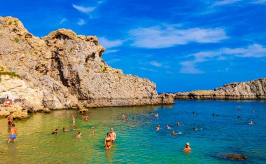 St Pauls Bay Lindos plaj manzarası turkuaz berrak su botu turistleri ve Rodos Yunanistan 'da güneş görüyor.
